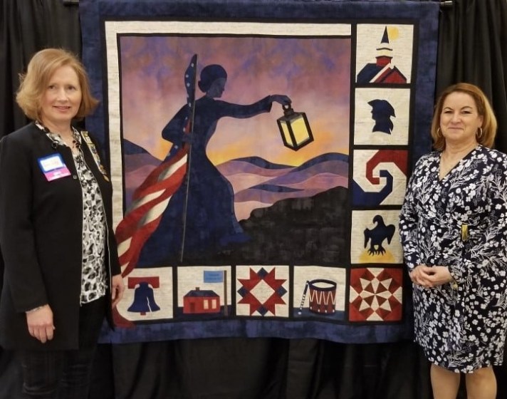 two women standing next to a homemade quilt