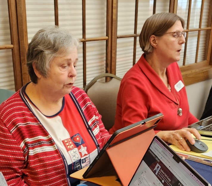 two women sitting behind a table answering questions about genealogy