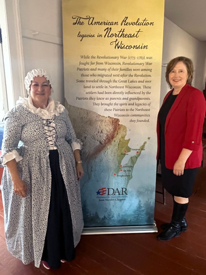 two women standing next to a poster about local legacies of the American Revolution