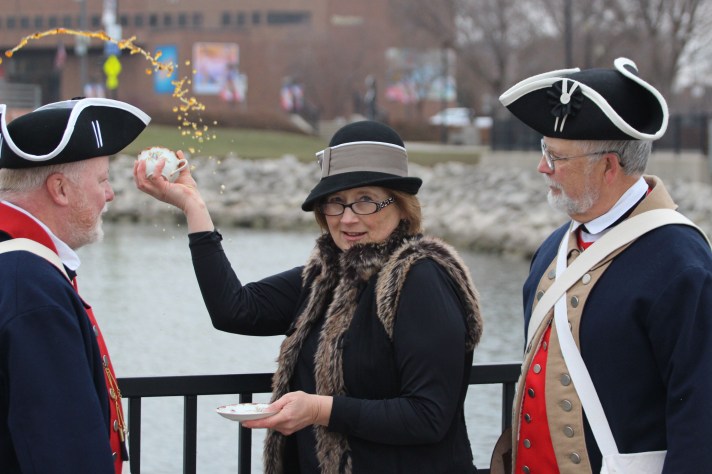 woman throwing tea into the river for the 250th anniversary of the Boston Tea Party