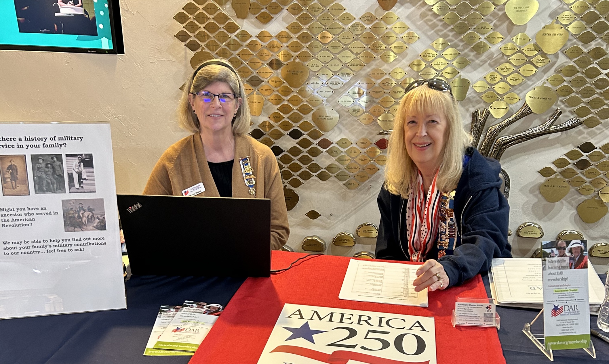 two women sitting at a table offering help at the America 250 booth
