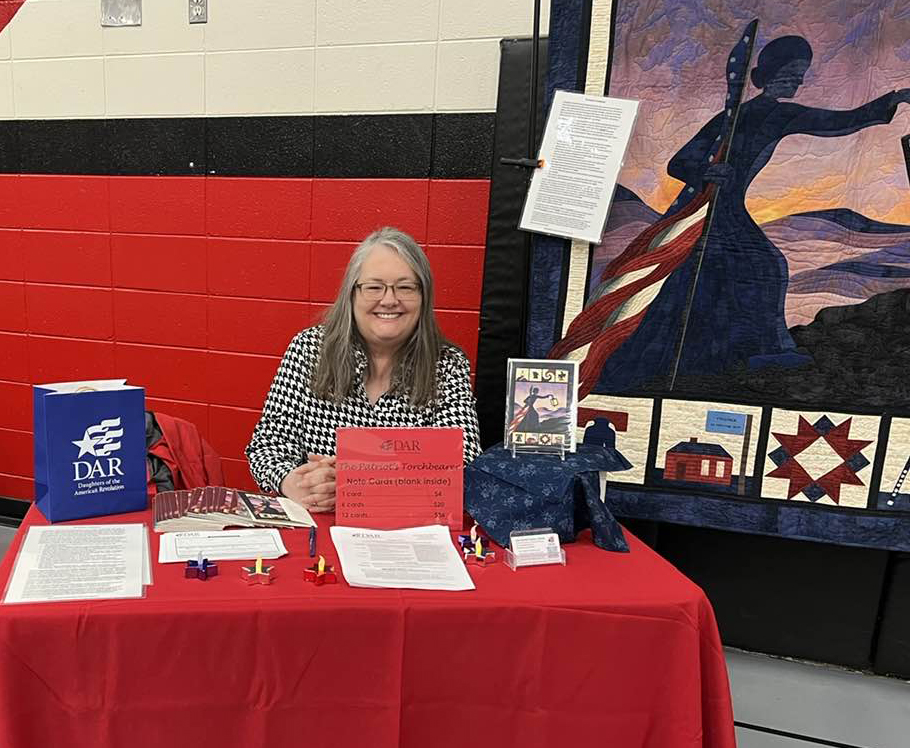 woman sitting at a table with the Jean Nicolet Chapter award-winning quilt
